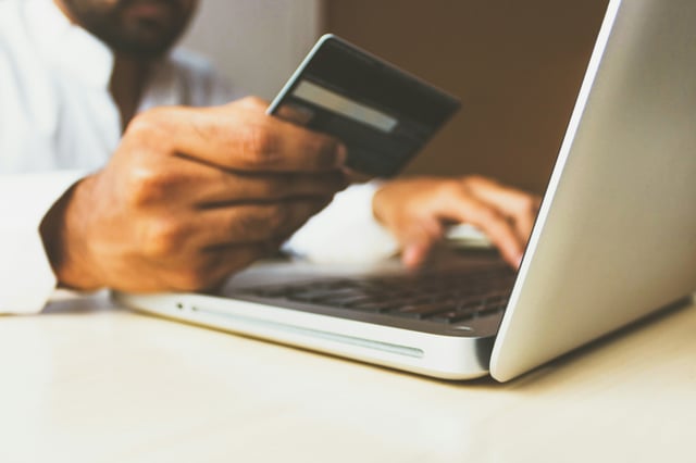 Iemand met een creditcard in de hand typt iets op een computer